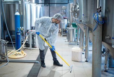 Professional industrial cleaner in protective uniform cleaning floor of food processing plant. Cleaning services.